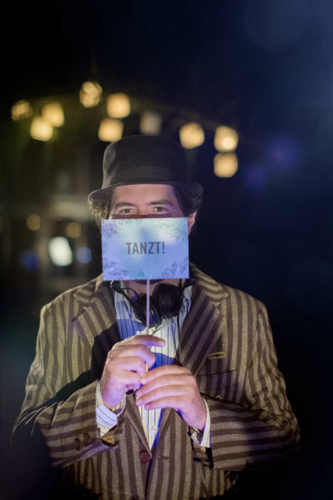 Portrait of event DJ Markus Rosenbaum holding a sign that reads Tanzt! in front of his face