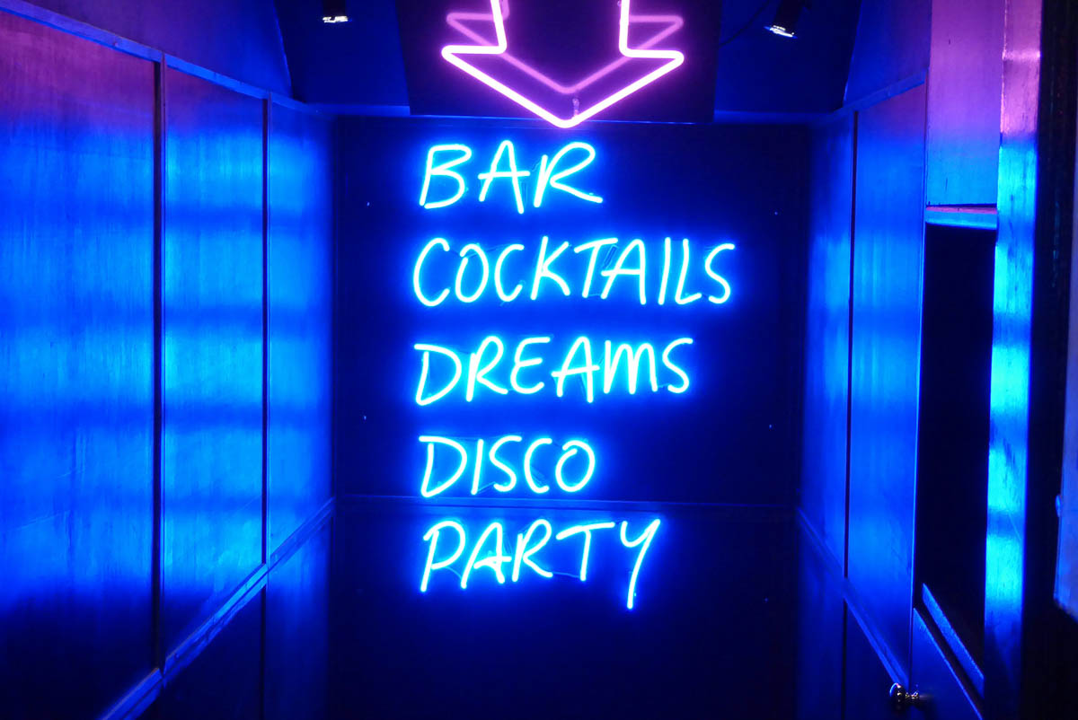 blauer Neon Schrifzug mit den Begriffen Bar, Cocktails, Dreams, Disco, Party