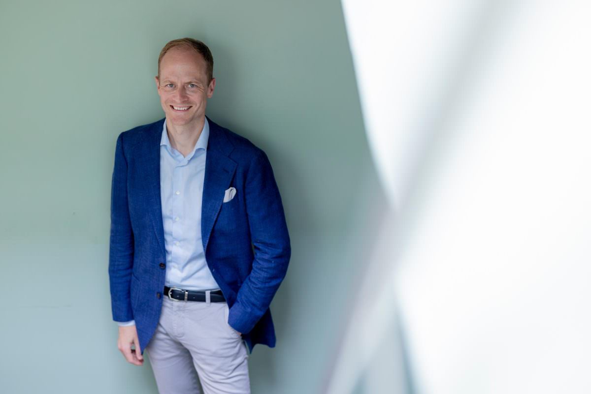 For the portrait, DJ Tobi has one hand in his pocket and is standing in front of a grey wall.