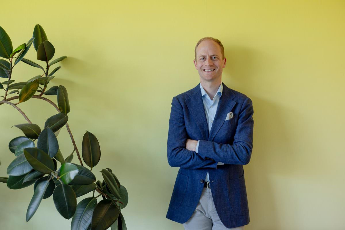 Half-body portrait of DJ Tobi standing with his arms crossed in front of a yellow wall.