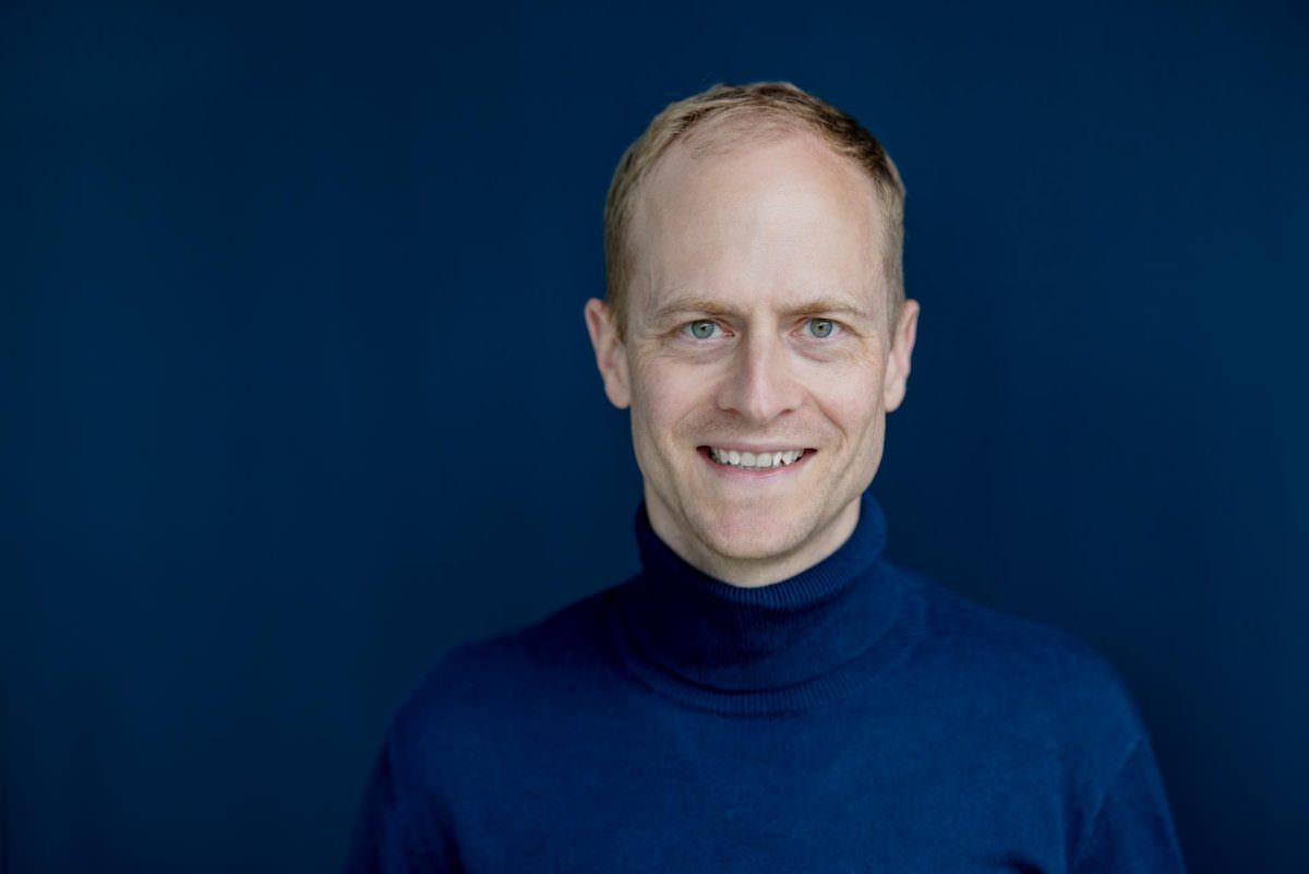 Close-up portrait of DJ Tobi standing in front of a dark blue wall