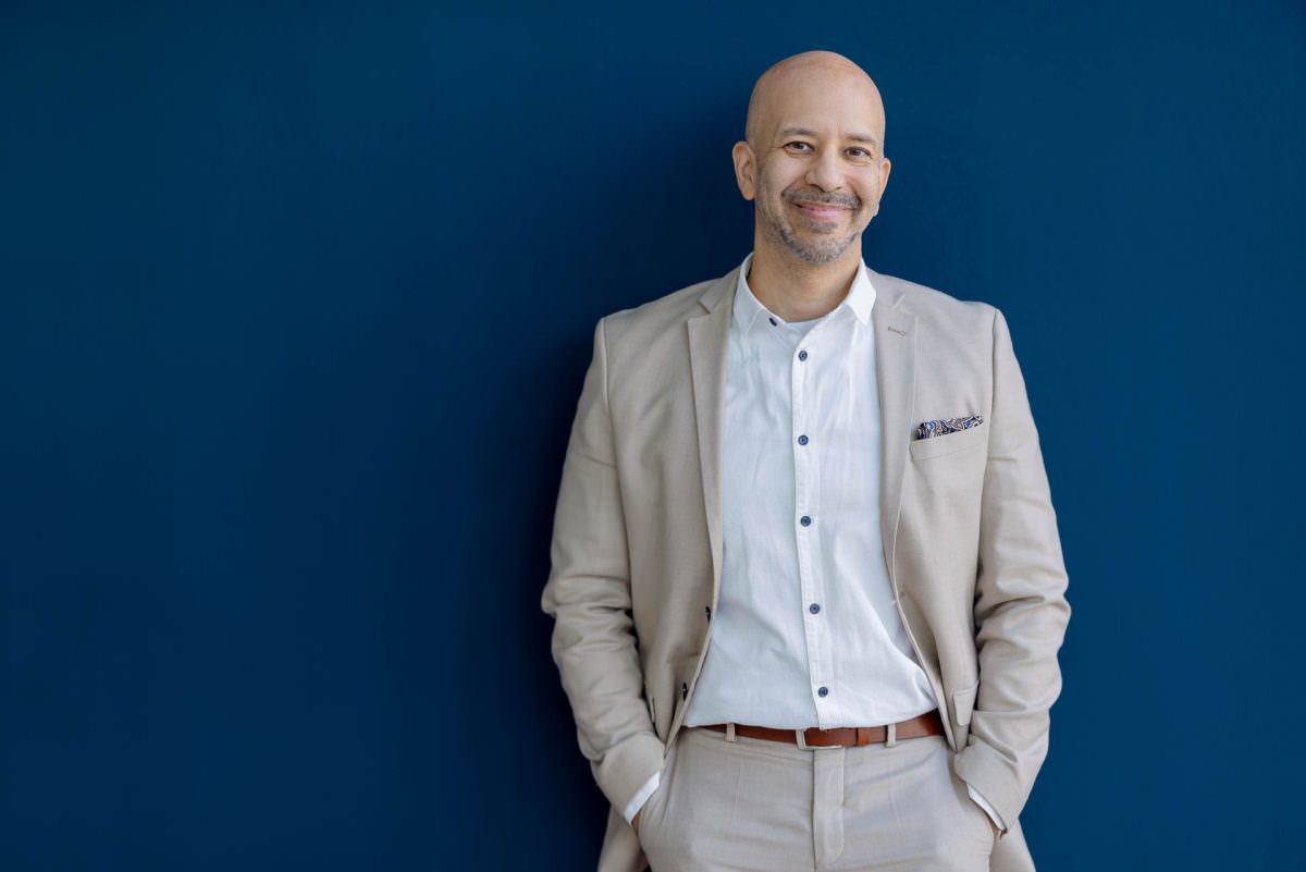 DJ Viru stands for his portrait in front of a dark blue wall with his hands in his pockets.
