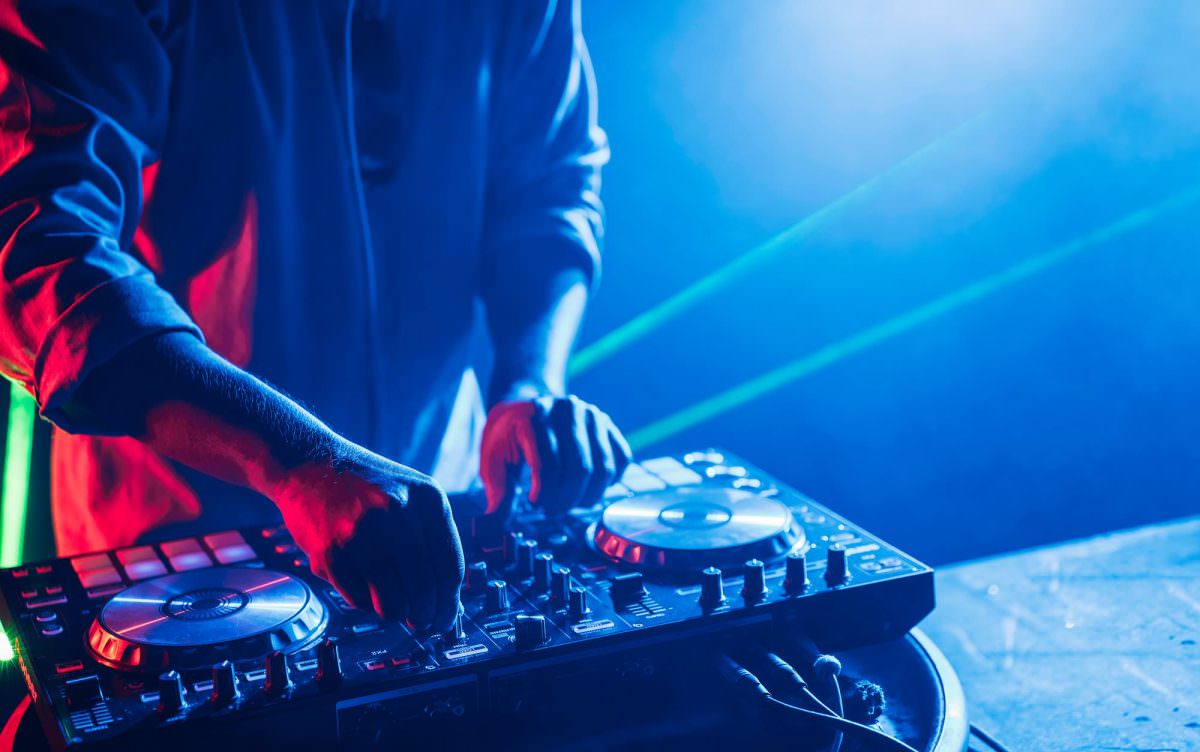 A DJ is mixing a song at his deck while playing at a party.