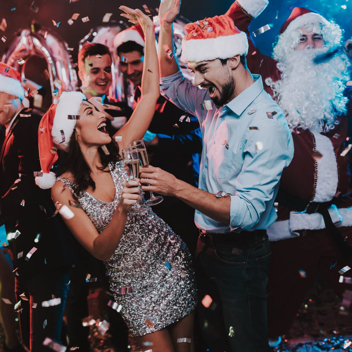 Gäste einer Weihnachtsfeier tragen Nikolausmützen und stoßen mit Sekt im Konfettiregen an